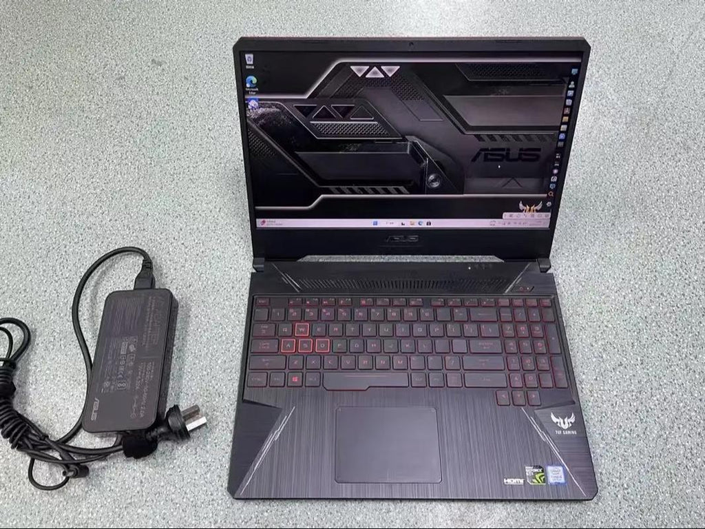 ASUS TUF Gaming 15-inch laptop with red accents and power adapter